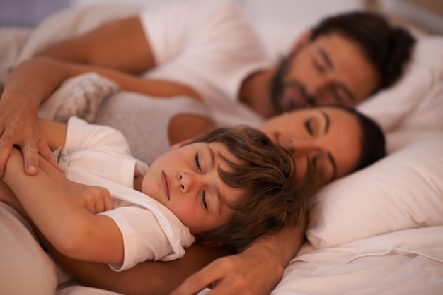 Ele sempre quer estar perto da mamãe e do papai Foto recortada de uma jovem família na cama juntos