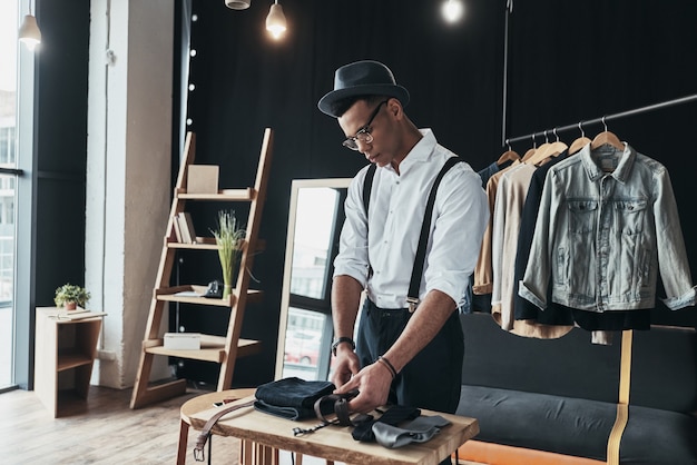 Ele tem um ótimo estilo. Jovem sério organizando roupas masculinas em pé no showroom