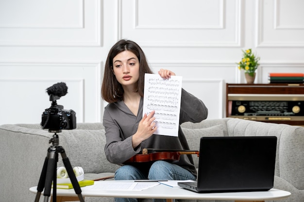 Elearning linda garota remotamente em casa dando aulas de violino com notas na câmera