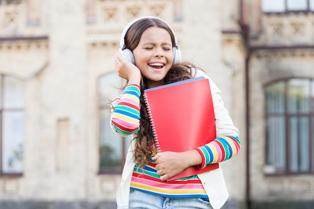 Elearning y métodos modernos Colegiala sostiene libros de trabajo y auriculares Tecnologías para estudiar Tecnologías modernas Educación a distancia Escuchar libros escolares Tecnologías digitales para el aprendizaje