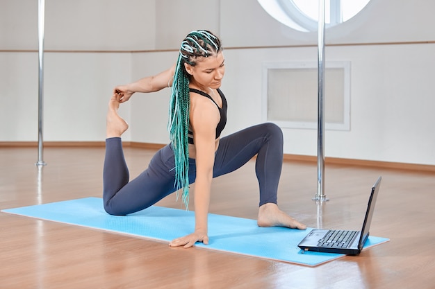 Elearning o educación a distancia de estiramiento, mujer de mediana edad viendo lecciones de flexibilidad corporal en línea usando una computadora portátil.