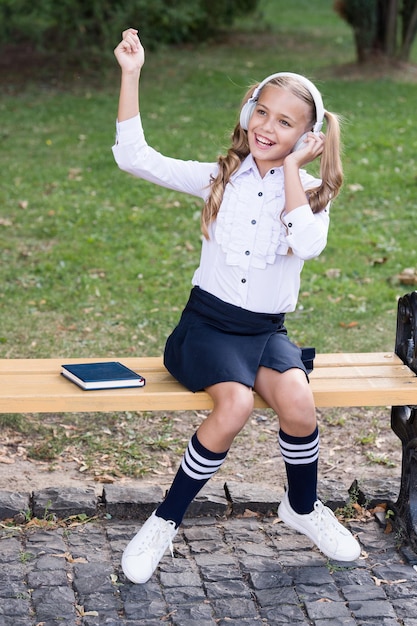 Elearning Vintage Kind Mode kleines glückliches Mädchen hören ebook alte Schulmusik zurück zur Schule mit Headset-Technologie Schulmädchen in stilvoller Retro-Uniform hören Hörbuch Tor zur Zukunft
