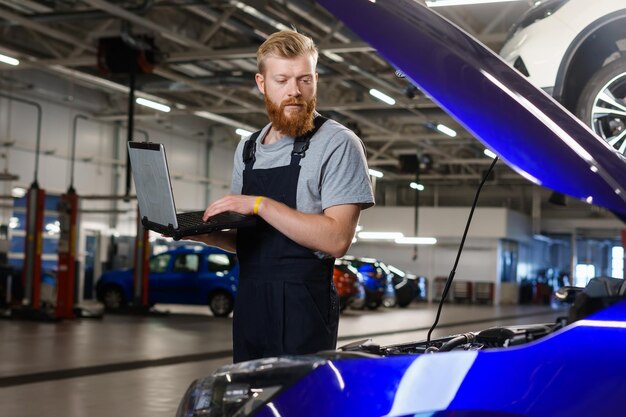 Un electricista automotriz masculino durante la solución de problemas en un automóvil con la ayuda de equipos profesionales