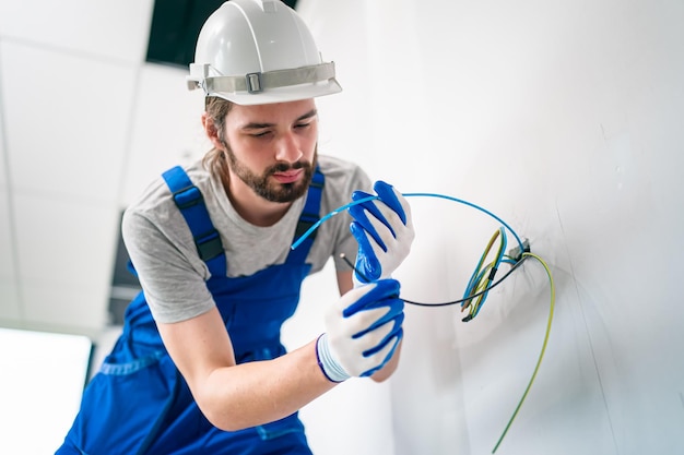 Un electricista está montando enchufes eléctricos en la pared blanca en el interior