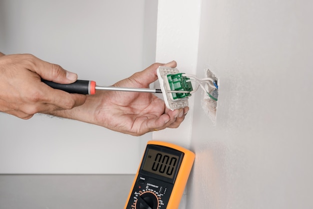 El electricista está utilizando un destornillador para conectar el cable de alimentación a la toma de corriente de la pared.