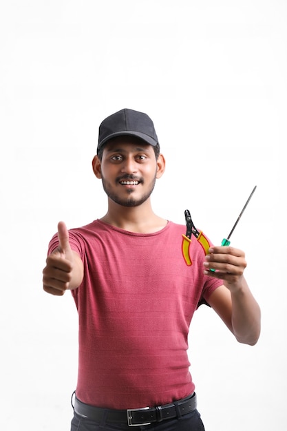 Electricista indio joven que sostiene las herramientas en la mano y que se coloca sobre el fondo blanco.