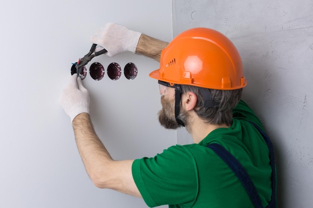 Un electricista instala enchufes en el apartamento. Un tipo con casco naranja hace electricidad.