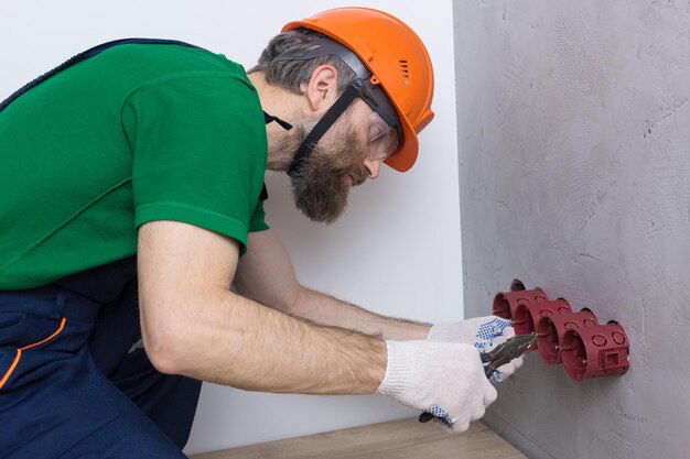 Un electricista instala enchufes en el apartamento. Un tipo con casco y overol hace electricidad.