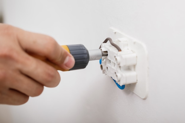 Electricista instalando toma de corriente en la pared con un destornillador. de cerca