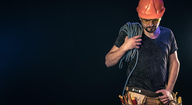 El electricista masculino con un cable eléctrico en un espacio de copia de fondo negro