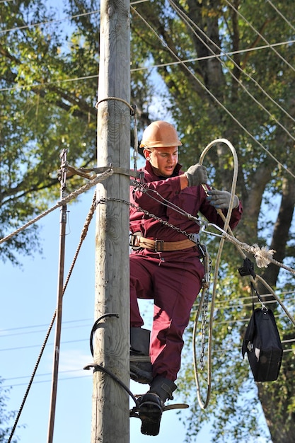 Un electricista en un poste de madera se prepara para reparar una línea eléctrica