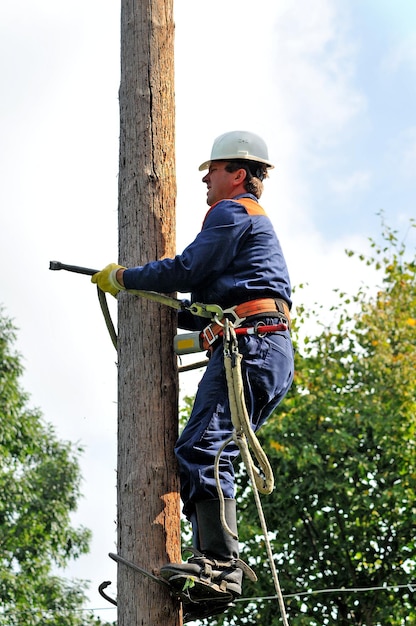 Un electricista sube a un soporte de madera para reparar una línea eléctrica