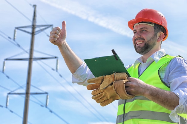 Electricista trabajando en un casco con guantes de pie en un campo