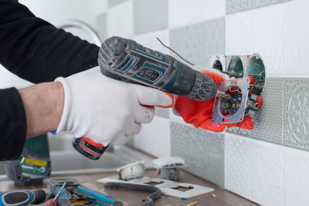 Electricistas instalando a mano toma de corriente en la pared con baldosas de cerámica con herramientas profesionales