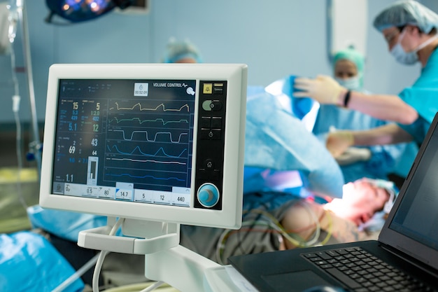 Electrocardiograma en la cirugía del hospital que opera la sala de emergencias que muestra la frecuencia cardíaca del paciente con un equipo borroso de cirujanos