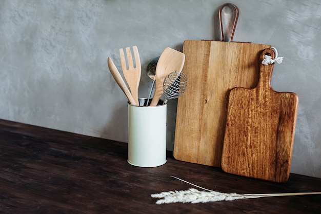 Electrodomésticos de cocina Metal y madera. tenedor, cuchara y espátula sobre una mesa de madera, contra una pared con textura gris.