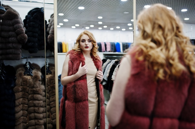 Elegancia chica rubia en abrigo de piel en la tienda de abrigos de piel y chaquetas de cuero.