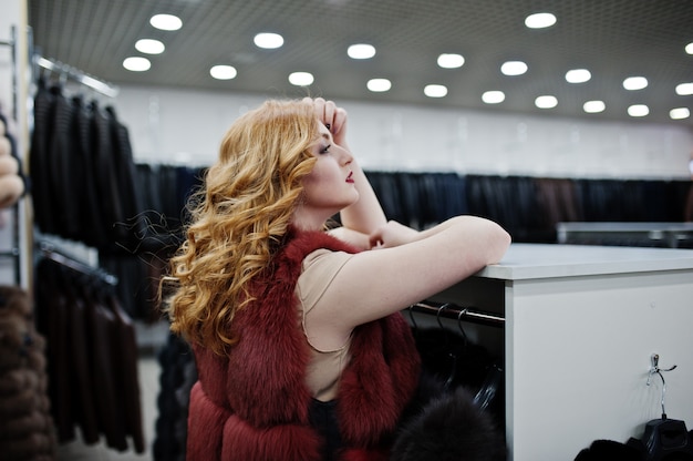 Elegancia chica rubia en abrigo de piel en la tienda de abrigos de piel y chaquetas de cuero.