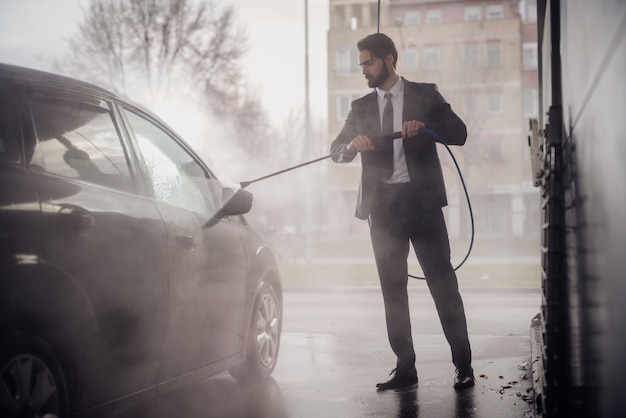 Elegant suted Mann, der sein Auto in der Autowäsche wäscht.