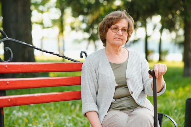 Elegante ältere Frau im Hemd sitzt an einem warmen Tag auf der Bank in einem Park