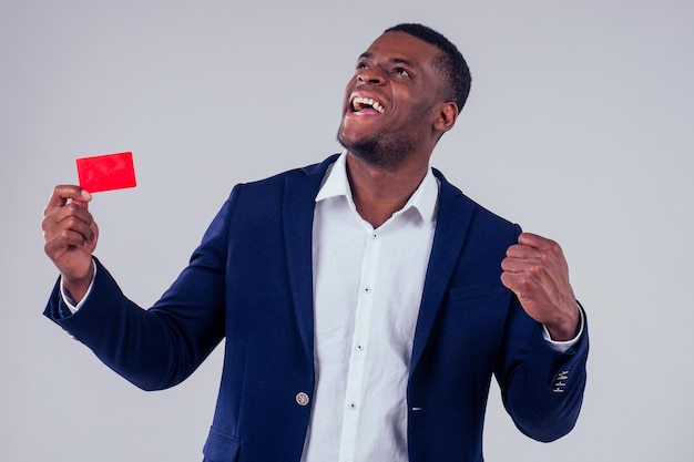 elegante afroamericano vestido con pantalones negros y chaqueta con un gran cuello de camisa con una tarjeta de crédito roja en el estudio con fondo blanco, insignia mi nombre es