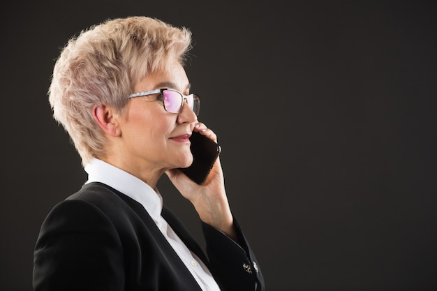 Elegante anciana con gafas y una chaqueta negra está llamando por teléfono