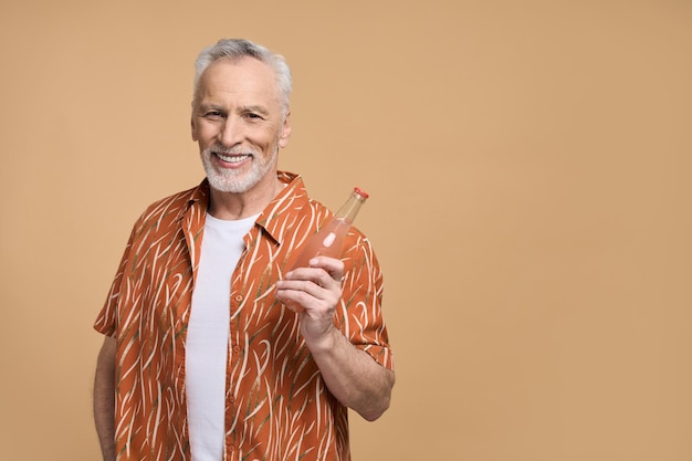 Elegante anciano barbudo con camisa naranja de verano sosteniendo refrescante limonada sonriendo a la cámara