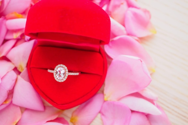 Elegante anillo de diamantes de boda en un joyero de corazón rojo sobre un hermoso fondo de pétalos de rosa rosa