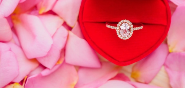 Elegante anillo de diamantes de boda en un joyero de corazón rojo sobre un hermoso fondo de pétalos de rosa rosa