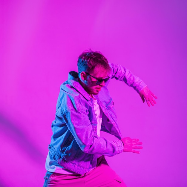 Elegante y apuesto joven bailarín de hip hop con ropa de mezclilla de moda bailando en el estudio con una creativa luz de neón rosa y azul