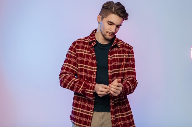 Elegante y apuesto joven hipster exitoso con ropa de moda que usa una camisa y mangas abotonadas en un estudio con luces creativas de colores