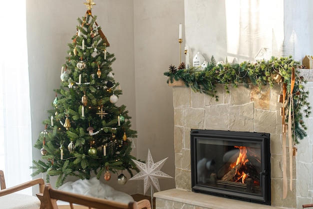 Elegante árbol de Navidad decorado con adornos antiguos y decoración moderna en la chimenea con campanas y cinta Moderna sala de estar navideña escandinava Nochebuena atmosférica