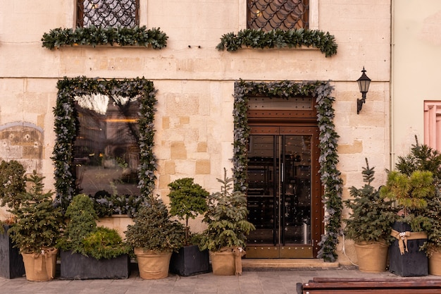 Elegante árbol de Navidad con frutos rojos, corona en las puertas y trineo de madera en la parte delantera de la tienda en el mercado navideño en la calle de la ciudad. Decoración de la calle de Navidad. Espacio para texto. Decoración rústica.