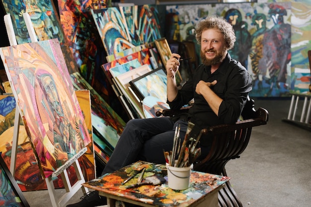 Elegante artista pintor barbudo fumando una pipa cerca de sus pinturas