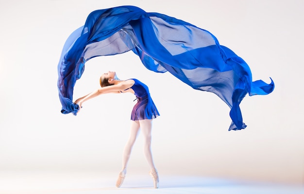 Elegante Ballerina in den Punkten tanzt mit einem sich entwickelnden blauen Tuch auf einem weißen Hintergrund