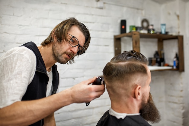 Elegante barbero corta a un hombre brutal con una espesa barba.