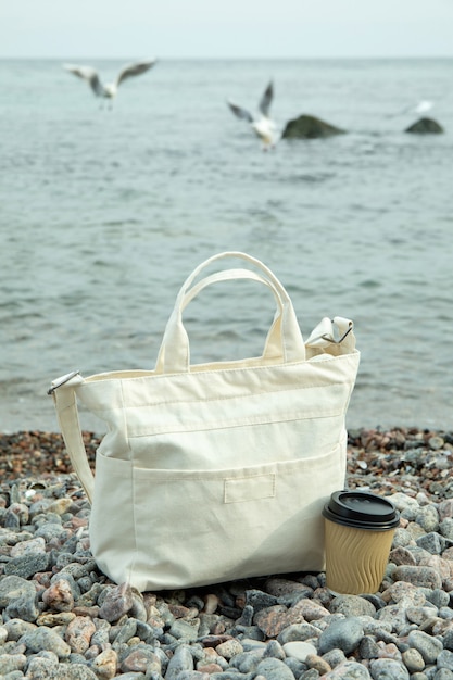 Elegante bolsa ecológica y vaso de papel al aire libre en la orilla del mar