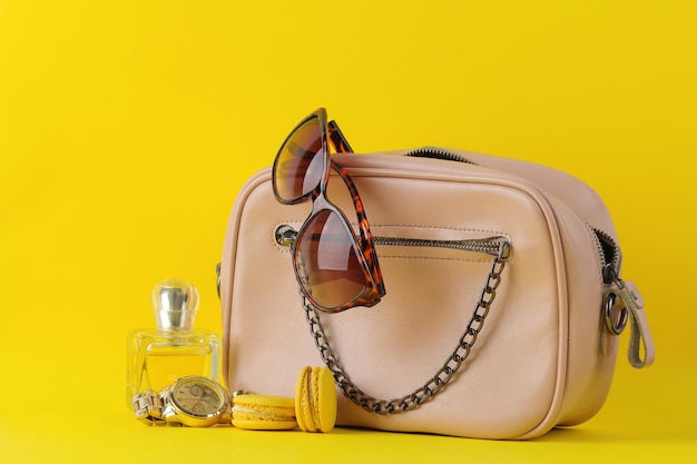 Elegante bolsa rosa elegante e cosméticos e acessórios femininos em um conceito de acessório feminino de fundo amarelo brilhante na moda