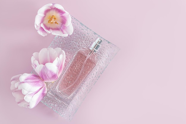 Una elegante botella de perfume de mujer se encuentra en una bandeja de vidrio en relieve con cabezas de flores de tulipán de primavera fondo lila vista superior una maqueta de espacio de copia