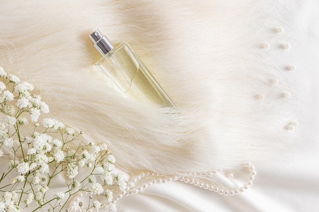 Una elegante botella de perfume de mujer está enterrada en un montón de perlas de piel beige y flores de gypsophila vista superior de fragancia costosa