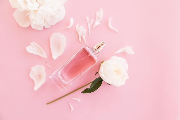 Una elegante botella de perfume de mujer o agua de tocador sobre un fondo rosa con hojas y un capullo de peonía vista superior una copia del espacio
