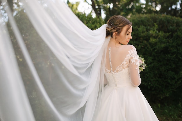 Elegante Braut im weißen Hochzeitskleid halten Blumenstrauß. Groß viel. Hintergrund des grünen Busches
