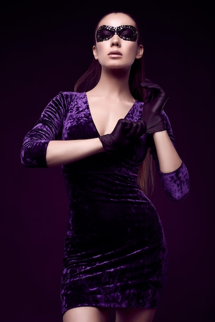 Elegante Brünette Frau in schönen lila Kleid und Pailletten Maske Handschuh nach oben