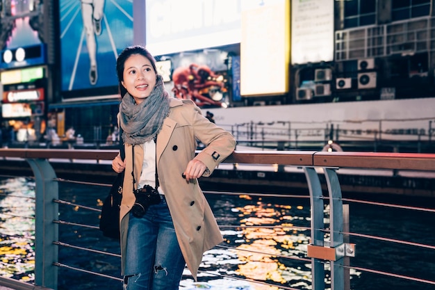 elegante bürodame trägt spiegelreflexkameras besichtigung dotonbori osaka japan in ihrer geschäftsreise reise freizeit. Junge Mädchen Touristen stehen entspannend neben dem Fluss. Nippon Running Man Werbung.