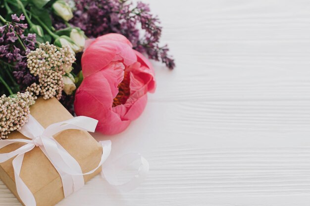 Elegante caja de regalo y ramo con peonía lila y rosas en espacio de madera blanca para texto