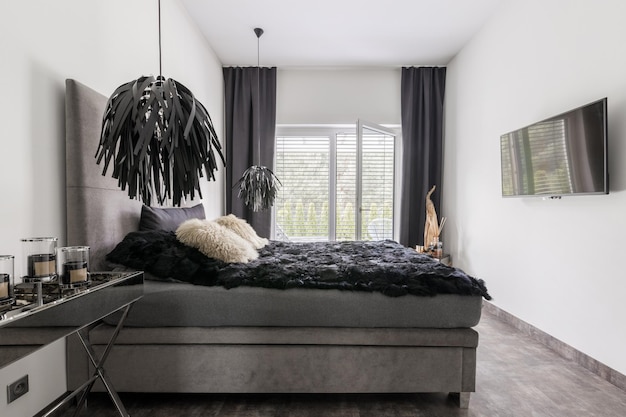 Elegante cama gris con ropa de cama negra en el interior de una habitación luminosa