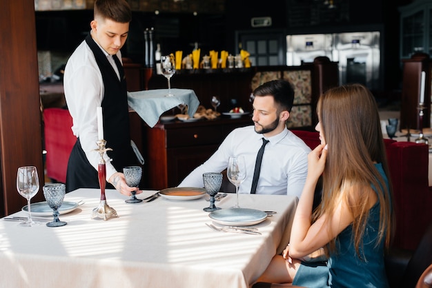 Un elegante camarero sirve a una pareja joven que tuvo una cita en un restaurante gourmet. Atención al cliente en el catering.