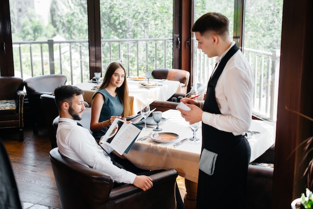 Un elegante camarero sirve a una pareja joven que tuvo una cita en un restaurante gourmet. Atención al cliente en el catering.