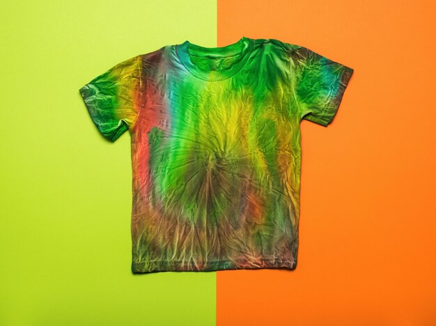 Una elegante camiseta tie dye pintada a mano sobre un fondo naranja y verde. Endecha plana.