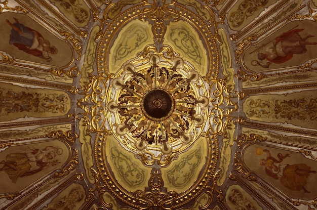 Elegante candelabro dorado colgando del techo adornado con frescos